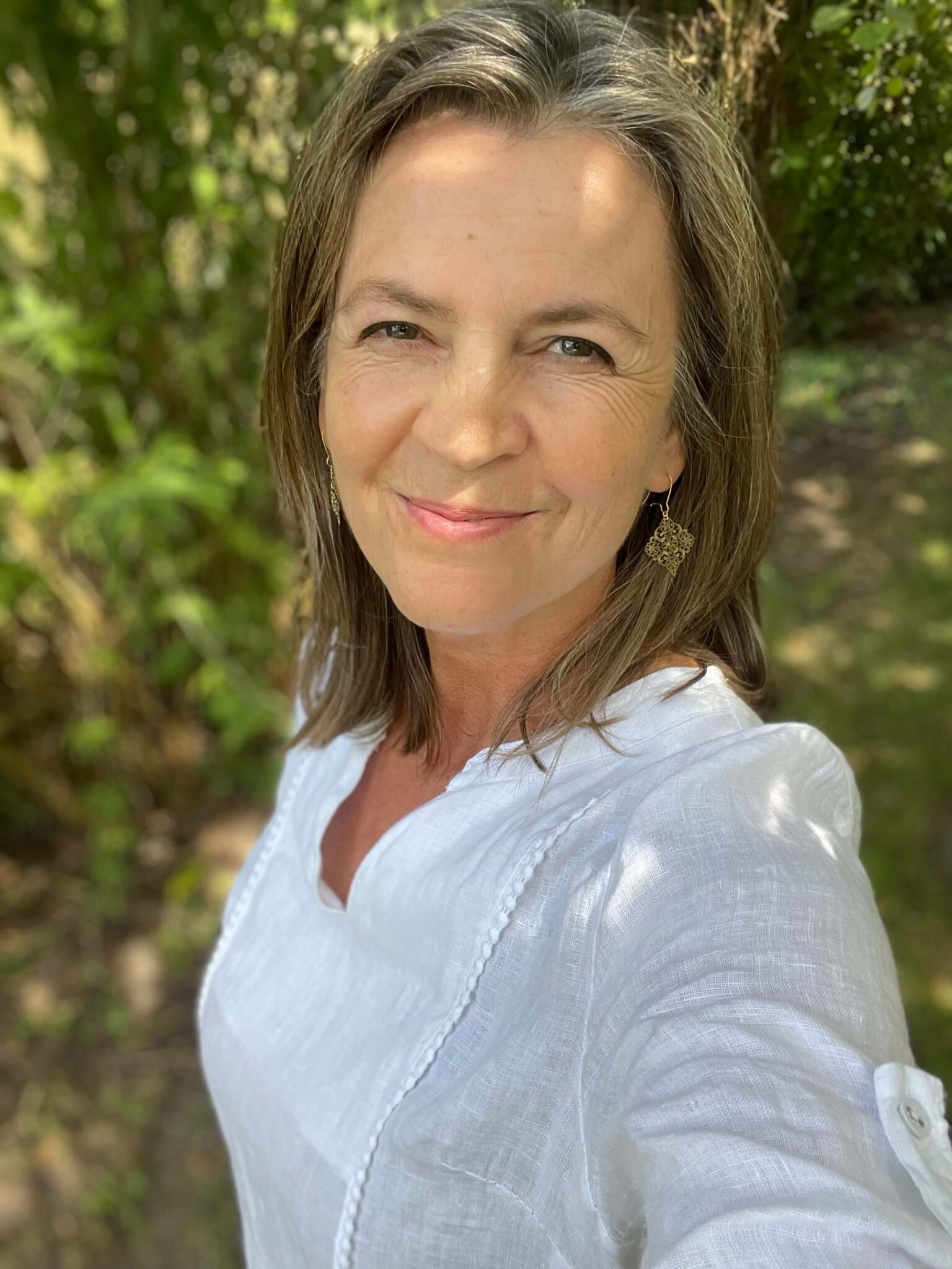 Karin Schaurhofer verbindet sich mit der geistigen Welt, um mit dir Wege aus der Krise zu finden. Dabei erfährst du, was dich blockiert, warum es gerade in deinem Leben nicht weiter geht und welche Weg du nun einschlagen sollst, um deinen Seelenplan zu erfüllen. diesem Bild ist das Portrait von Karin Schaurhofer zu sehen, sie trägt ein weisses Leinenkleid, dahinter ist ein grüner Park zu sehen, verschwommen