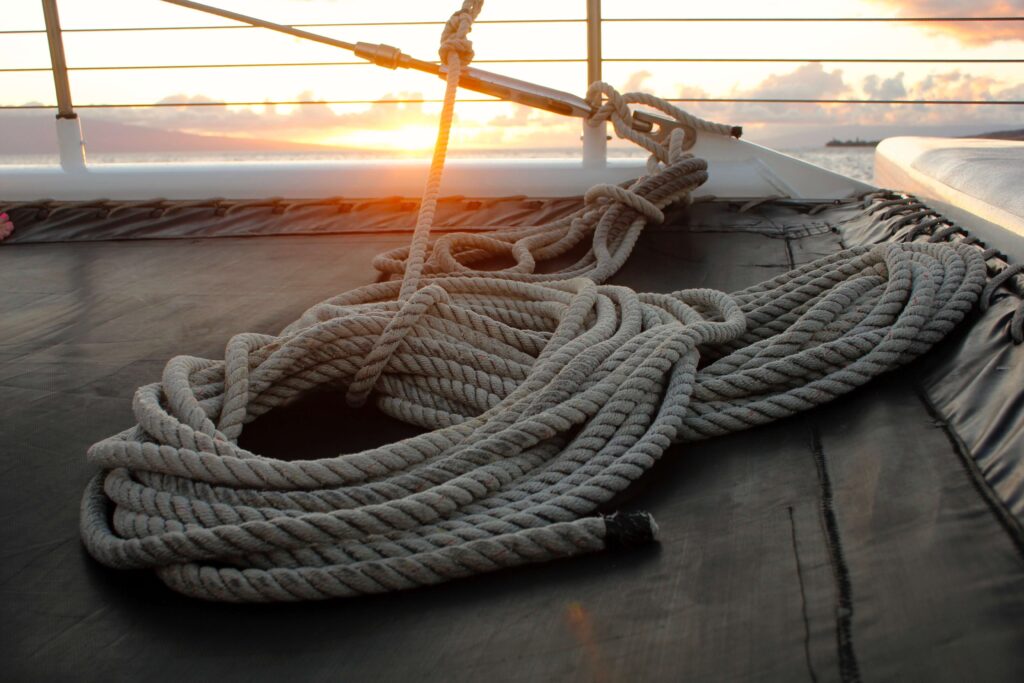 ein Seil liegt angeknotet auf einem Segelboot zusammengerollt , im HIntergrund ist ein Sonnenuntergang zu sehen.