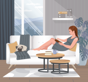 eine Frau sitzt auf der Couch und liest, zu ihren Füßen schläft eine Katze