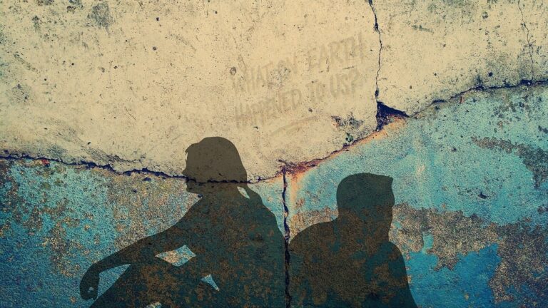 zwei Menschen sitzen am Boden, mit dem Rücken zueinander und schauen weg